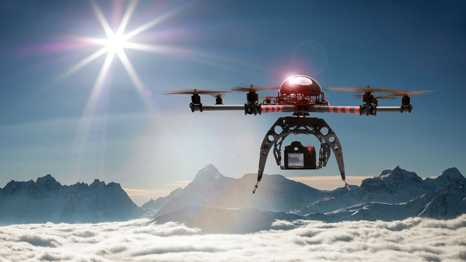 Eine Drohne fliegt über ein Wolkenmeer, im Hintergrund Berge.