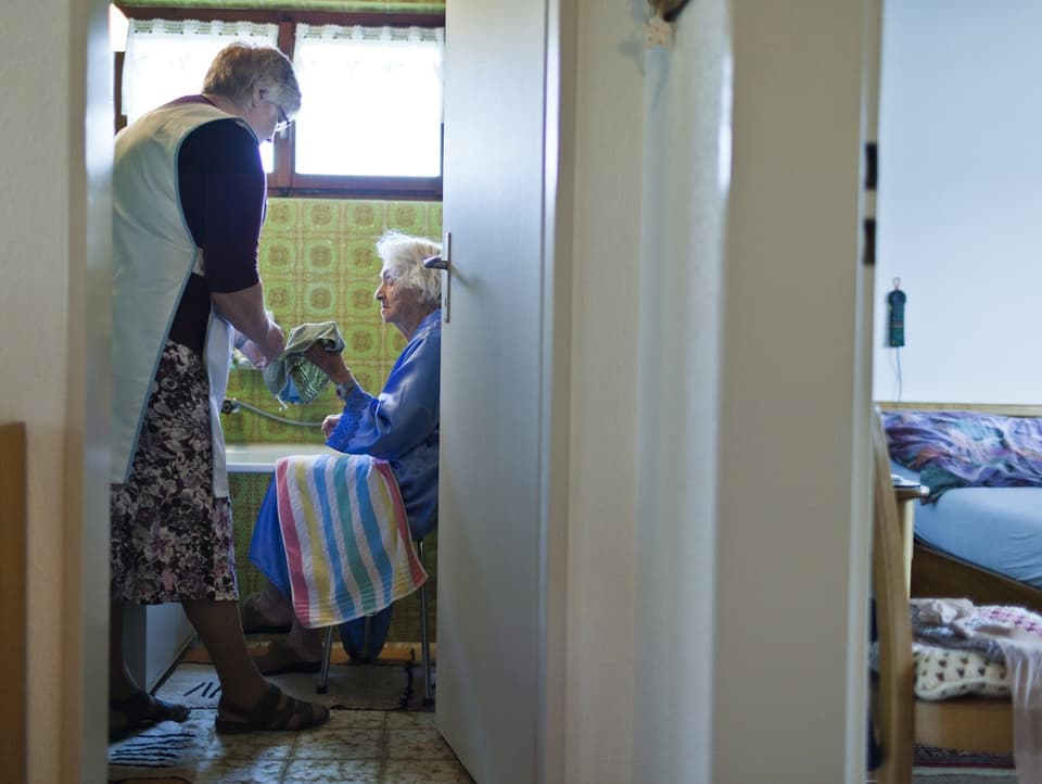 Eine Frau hilft einer älteren Frau, die neben einer Badewanne sitzt