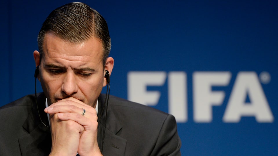 Markus Kattner stützt seinen Kopf auf zwei gefalteten Händen vor einem Fifa-Logo