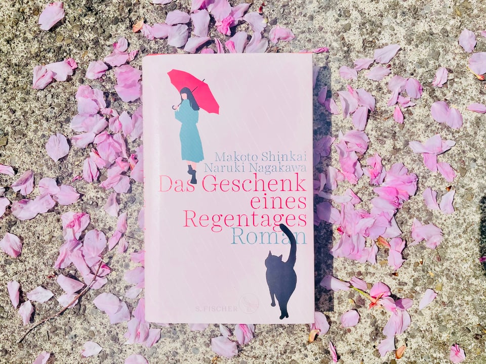 Der Roman «Das Geschenk eines Regentages» von Makoto Shinkai und Naruki Nagakawa liegt auf Kirschblüten