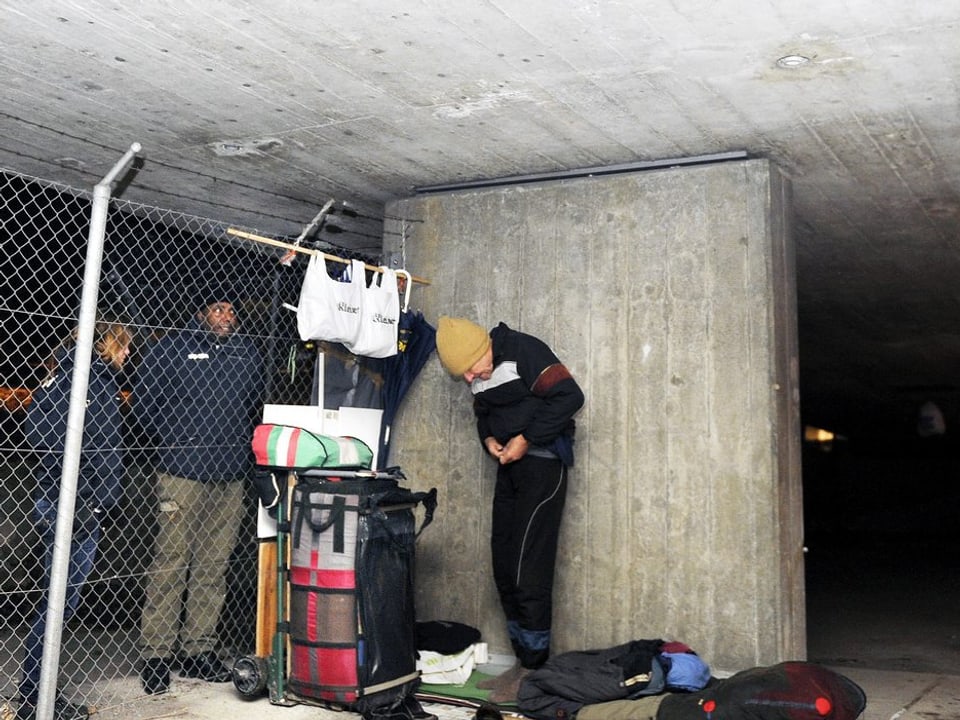 Ein Mann bereitet neben Angehörigen der SIP (Sicherheit, Intervention, Prävention, Stadt Zürich) seine Schlafstätte vor unter einer Brücke in Zürich.