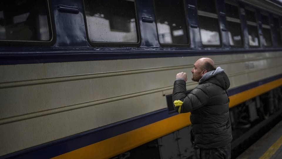 Ukrainischer Mann mit Glatze blickt aus Bahnhofsbahnsteig in Zugfenster.