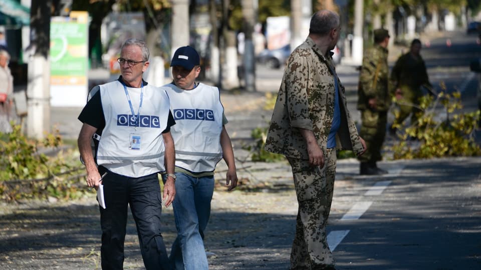 Zwei OSZE-Mitarbeiter überqueren eine Strasse. 