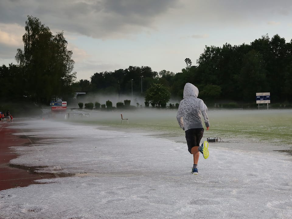 Eine Frau rennt auf einem roten Sportplatz davon, der Platz ist aber kaum noch rot, sonder weiss vor lauter Hagelkörnern. 