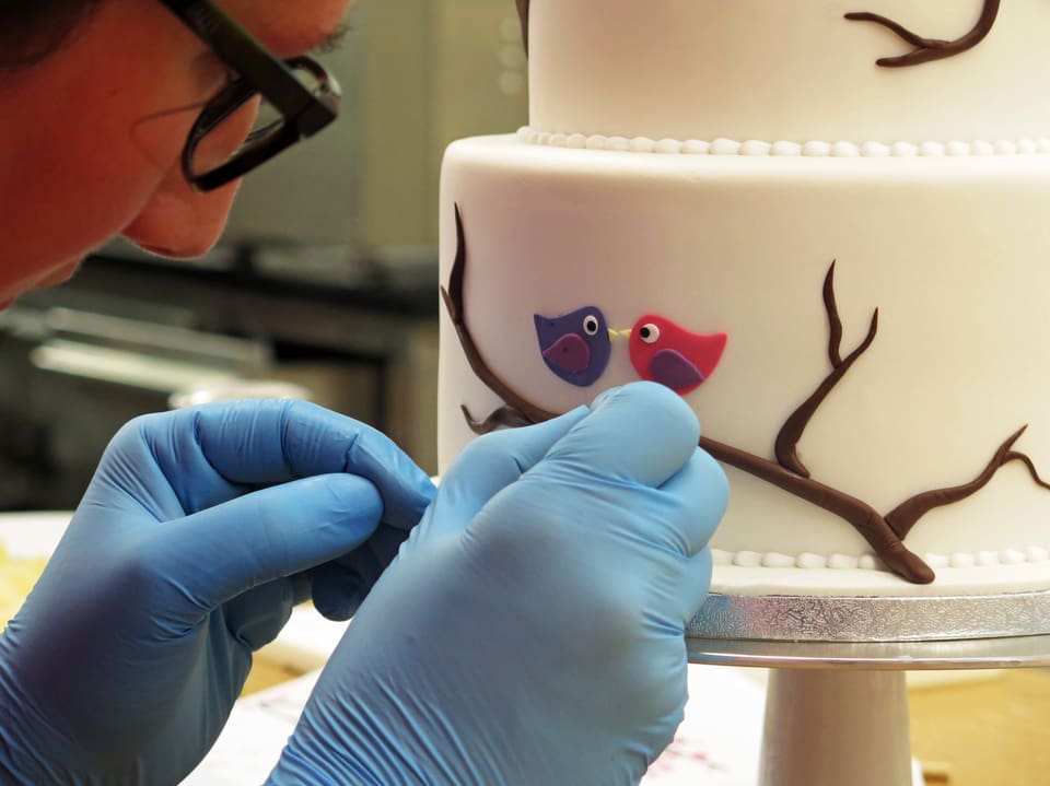 Törtlifee arbeitet mit Handschuhen an Detail der Torte