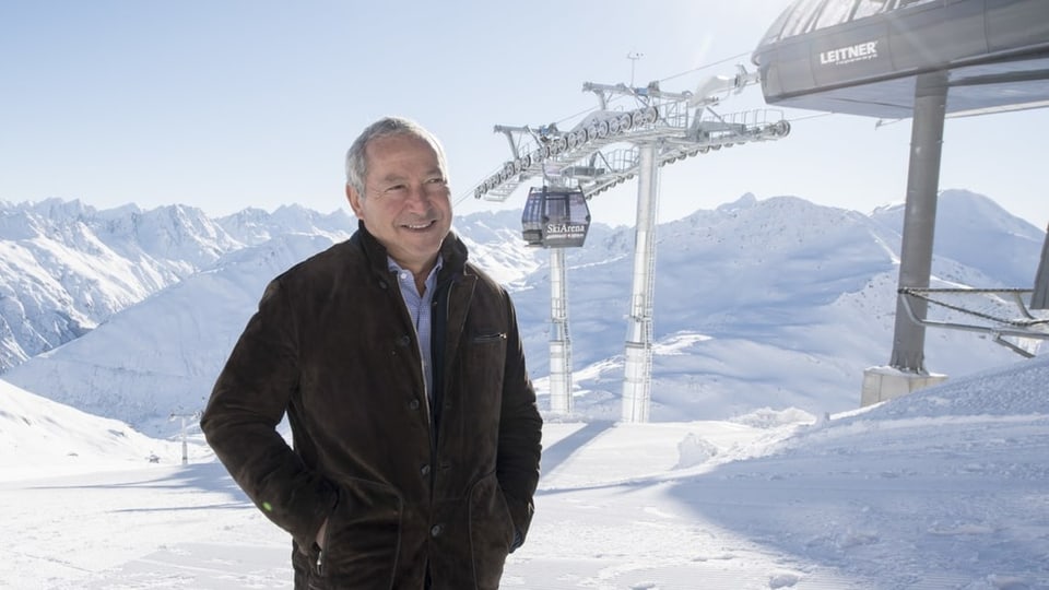 Sawiris steht vor den Schneebergen. Im Hintergrund eine Gondelbahn. 