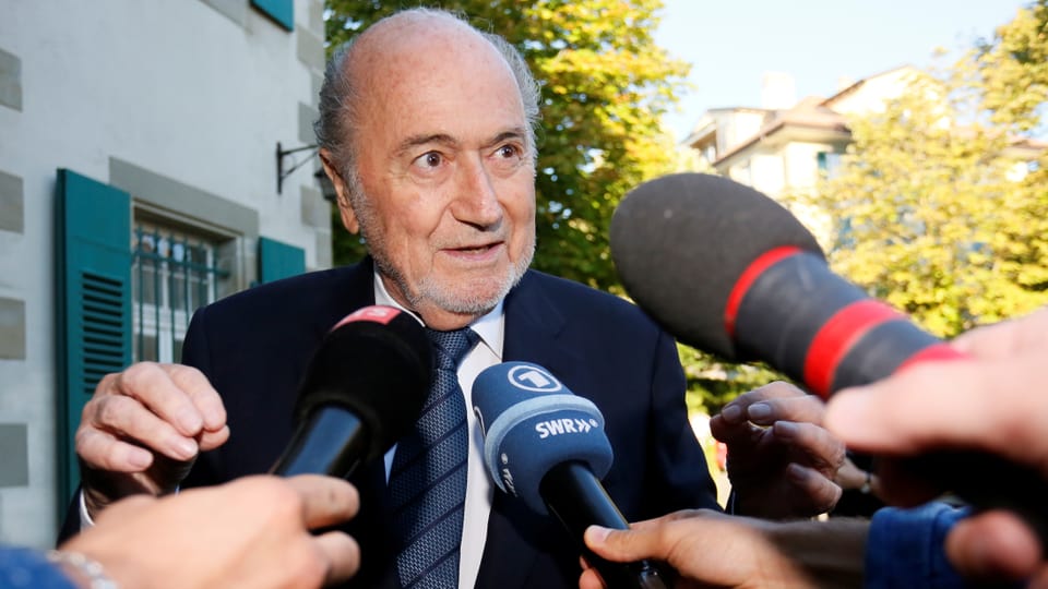 Blatter spricht in ihm entgegengehaltene Medien-Mikrofone.