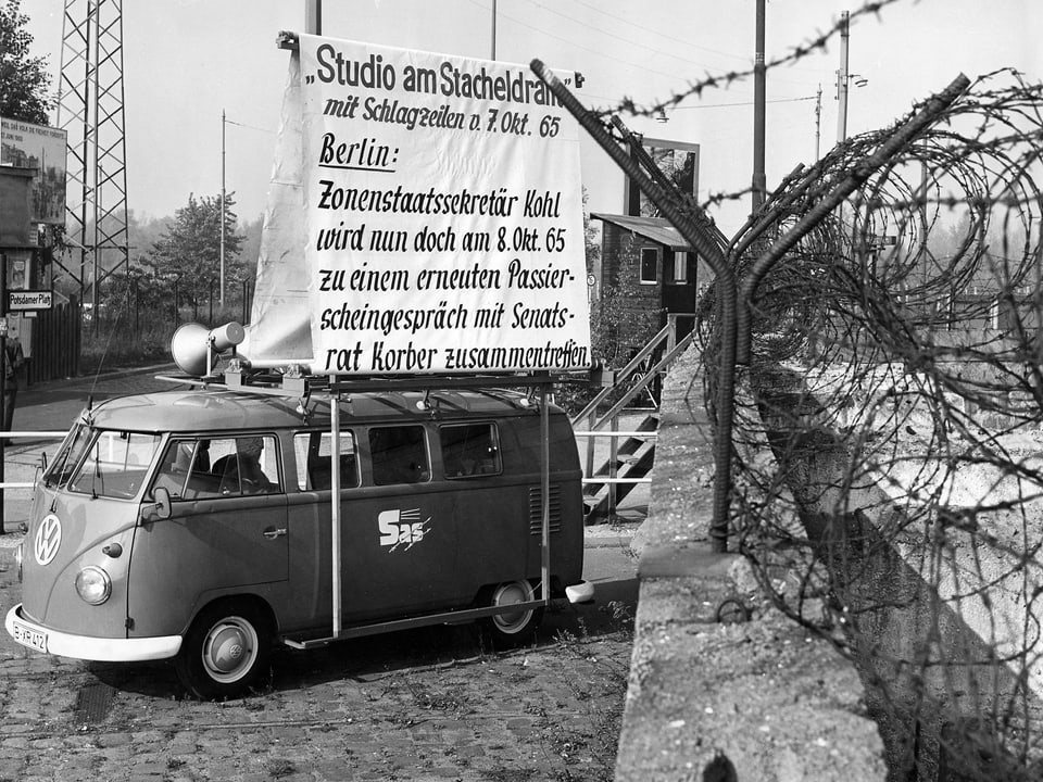 Bus mit Lautsprechern auf dem Dach steht neben Berliner Mauer