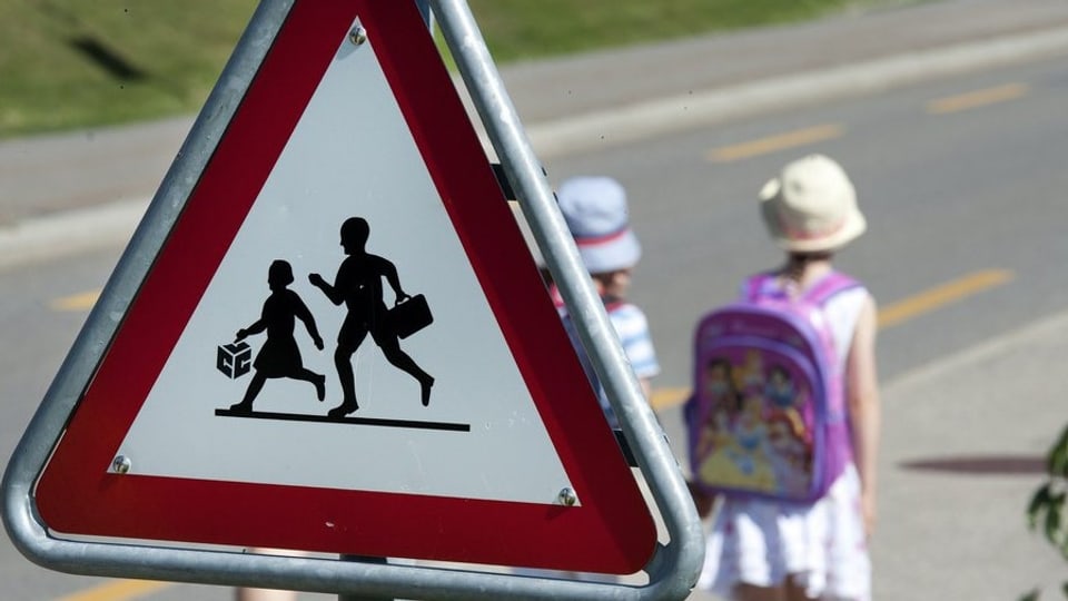 Schulweg-Schild mit Schülern im Hintergrund.