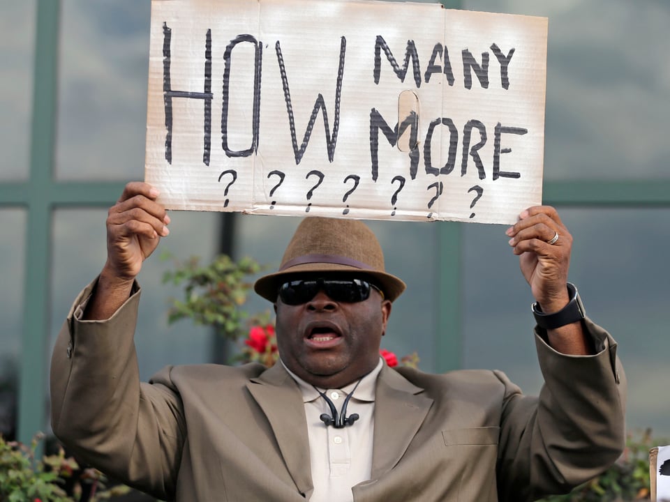 Ein Mann hält ein Schild mit der Aufschrift «How many more???????»