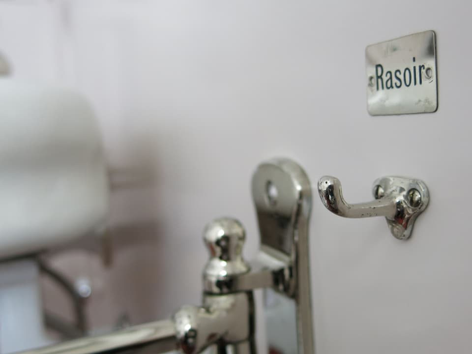 Ein alter Haken im Badezimmer mit einem Schild, auf dem «Rasoir» steht.