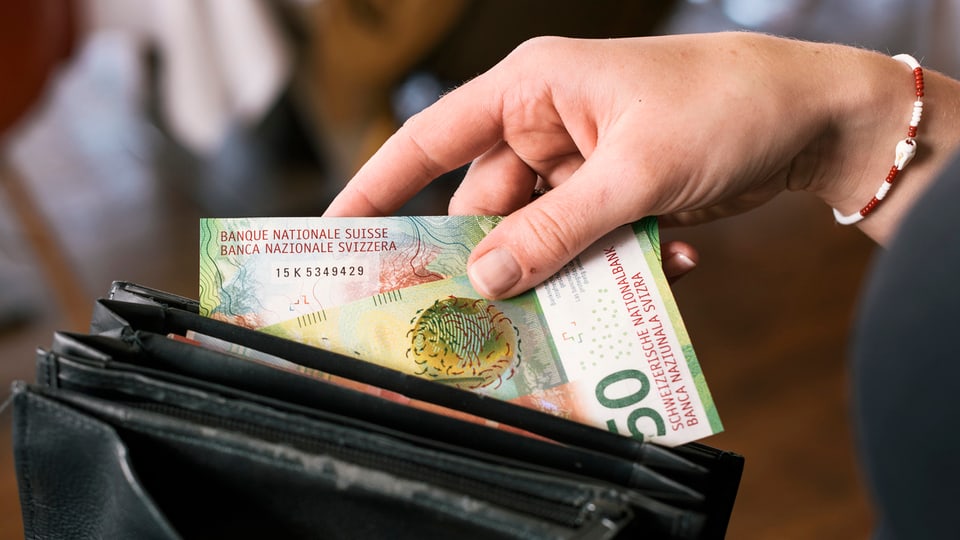Frauenhand steckt Banknoten in ein Portemonnaie