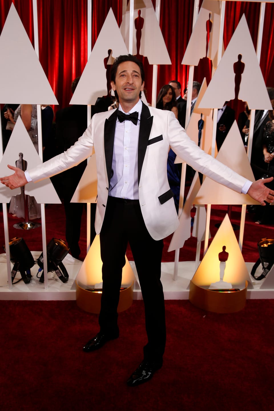 Adrien Brody posiert in weissem Kittel auf dem roten Teppich bei den Oscar-Verleihungen.