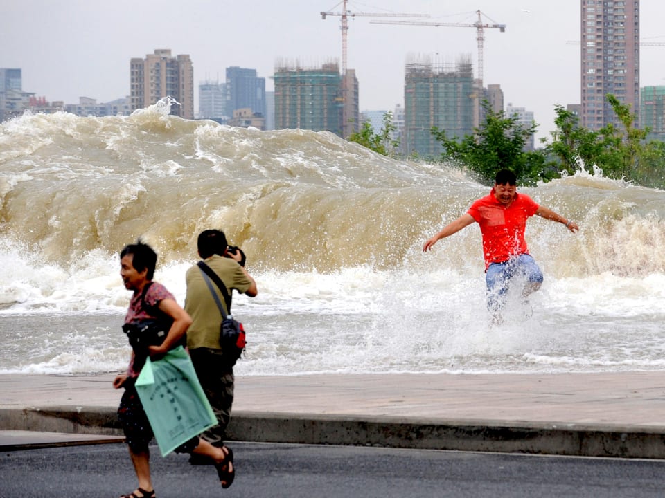Ein Mann macht ein Foto von einem anderen Mann, der vor der Welle im Wasser steht.