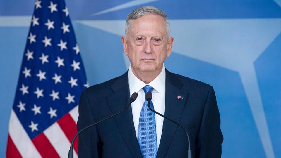Mit geschlossenem Mund ernstem Gesicht vor einer US-Flagge am Rednerpult des Nato-Sitzes.