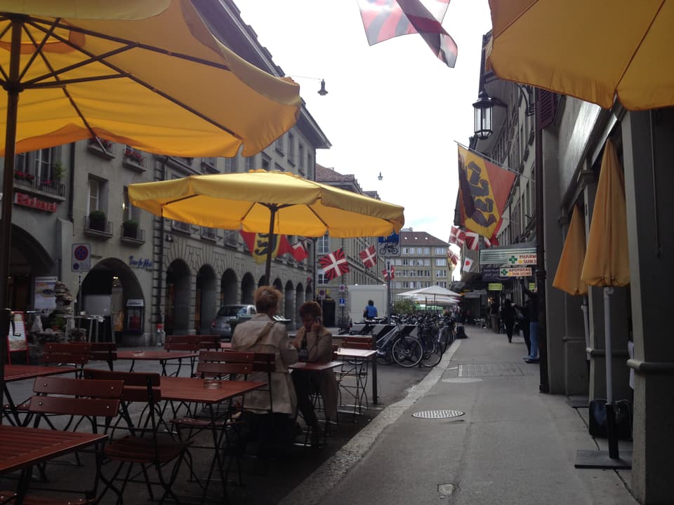 Aussentische eines Restaurants, gelbe Sonnenschirme, Berner Flagge.