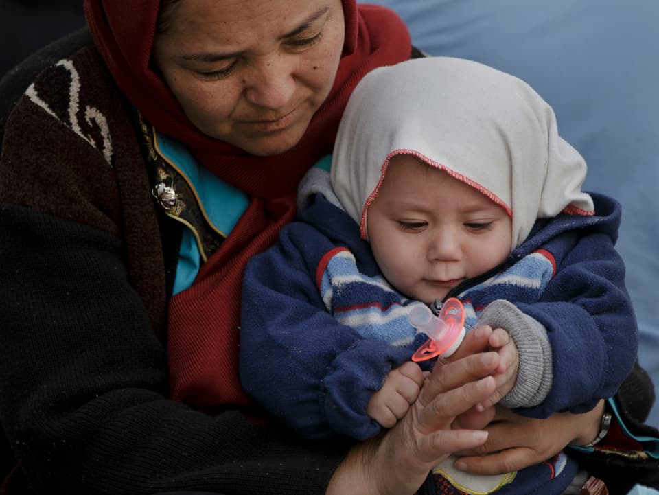 Eine Frau hält ein Kleinkind im Arm, das mit einem Schnuller spielt.