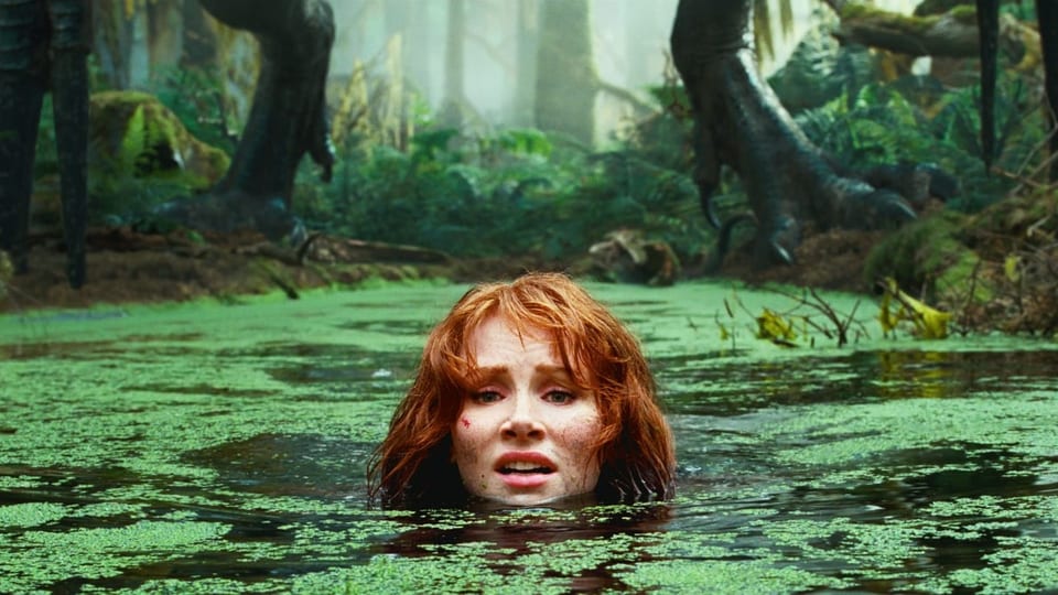 Eine Frau schwimmt in einem Tümpel voller Pflanzen, im Hintergrund die Beine eines Dinosauriers.