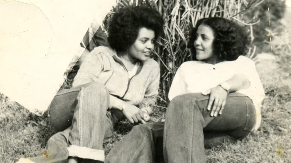 Zwei Frauen mit Jeans und weissem Pulli liegen in einer Wiese.