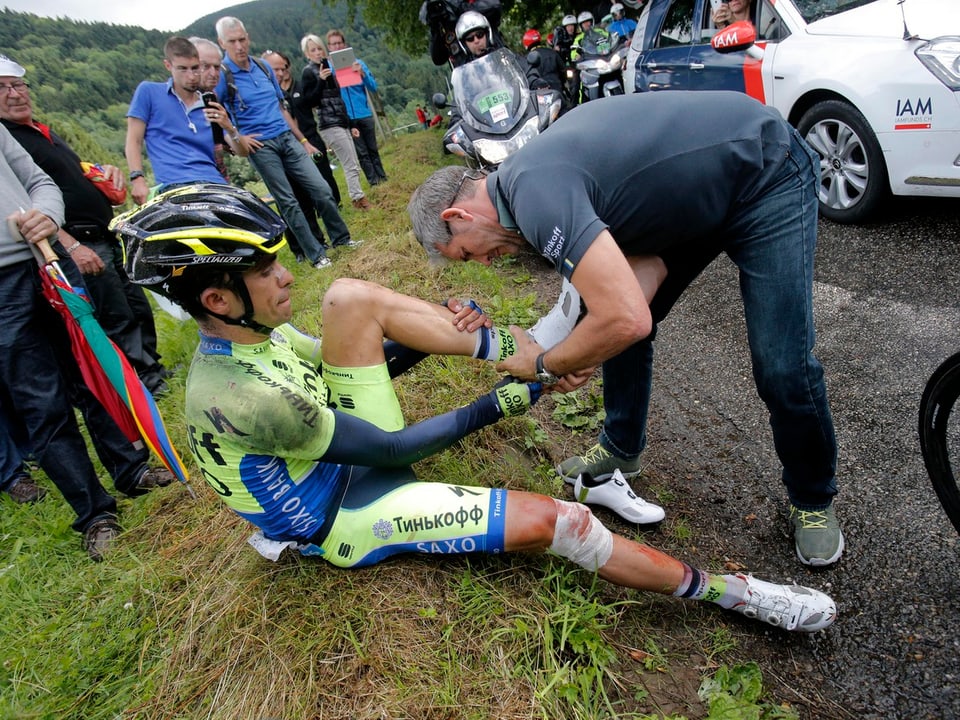 Alberto Contador sitzt nach seinem Sturz am Strassenrand und wird von einem Betreuer versorgt.