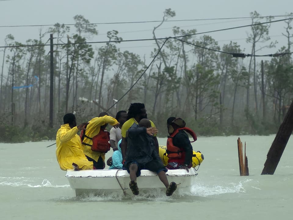 Mehrere Menschen auf einem kleinen Boot inmitten Überschwemmung.
