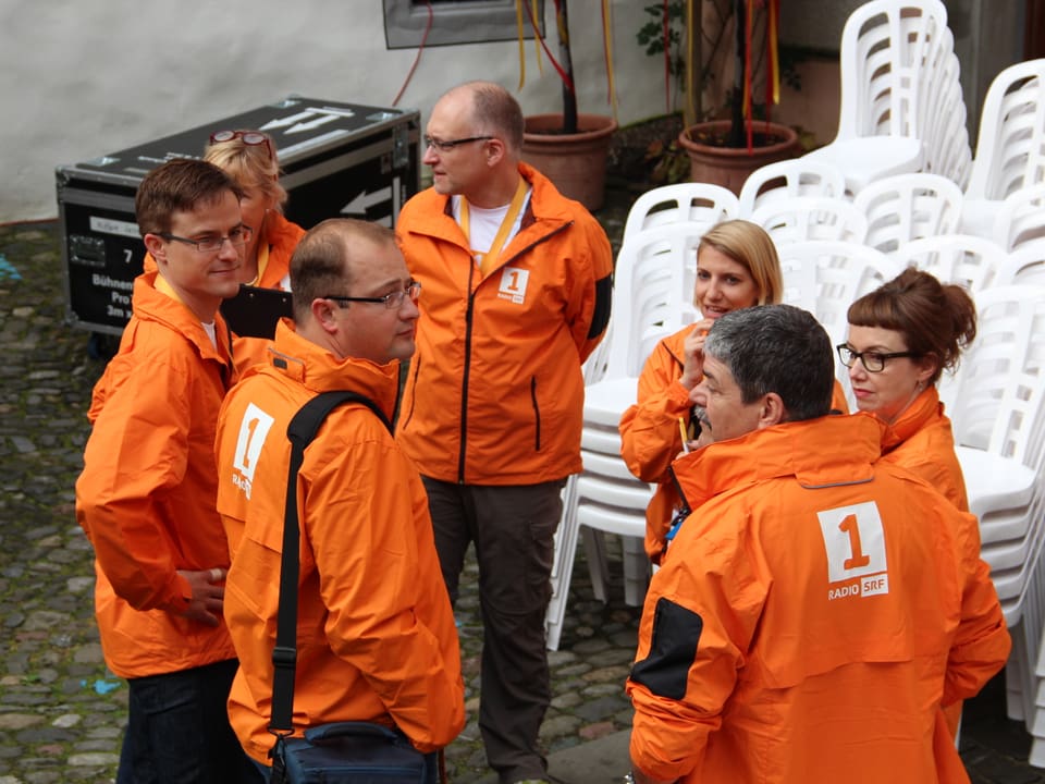 Teambesprechung auf dem Platz. Alle in orangen Radio SRF 1-Jacken gekleidet.