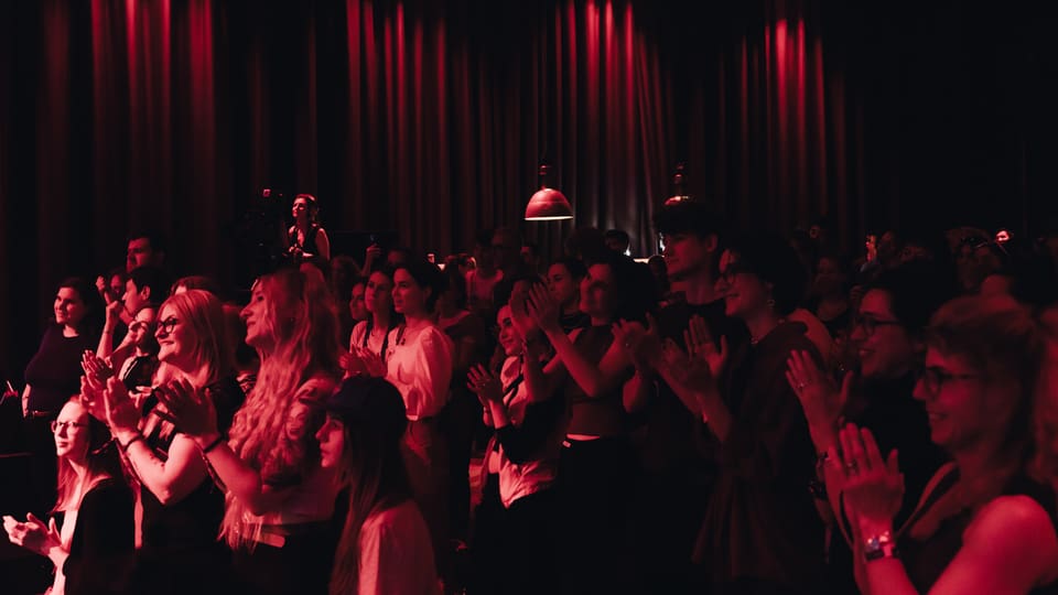 Menschenmenge klatscht bei einem Konzert in rotem Bühnenlicht.