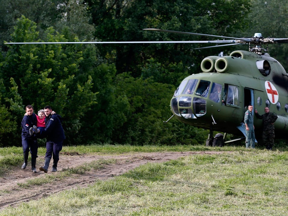 Serbische Polizisten tragen eine alte Frau aus einem Helikopter.