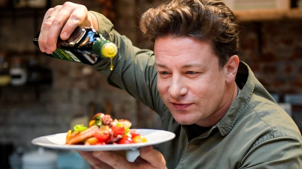 Ein junger Mann träufelt Olivenöl auf einen Teller.