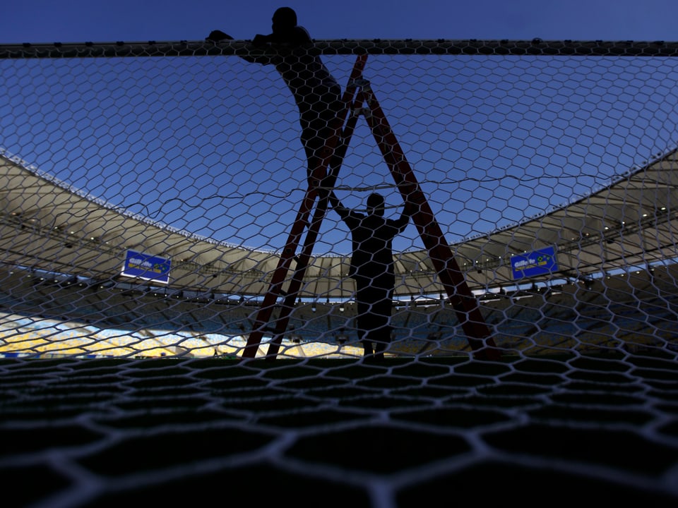 Zwei Arbeiter stellen gerade ein Fussballnetz in einem Fussballstadion in Rio auf. 
