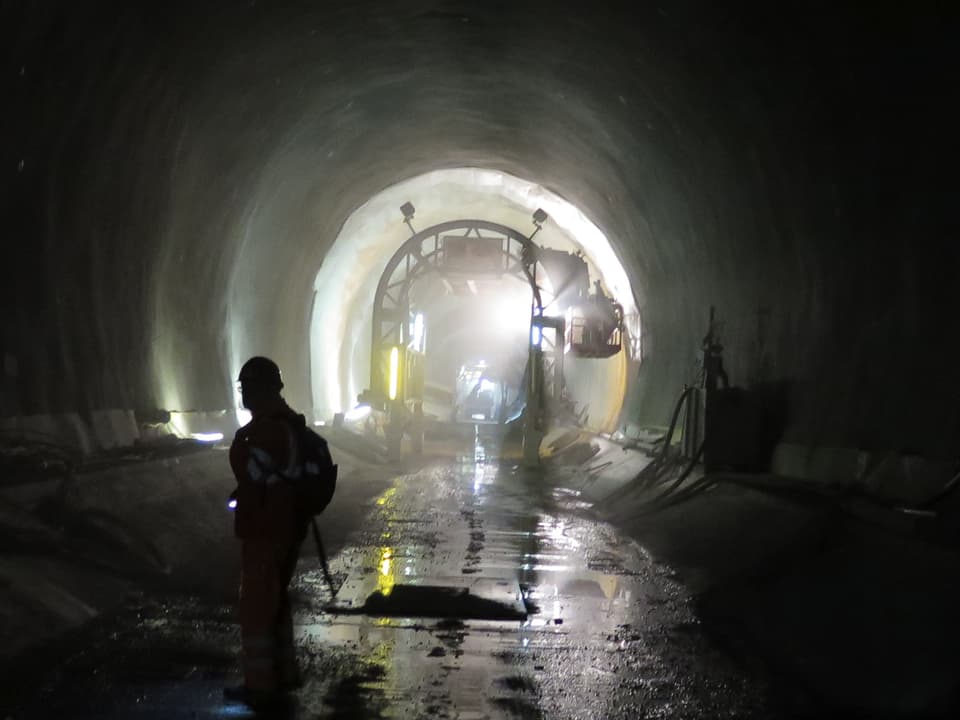 Im Vordergrund des ceneri-Tunnels steht ein Arbeiter, im Hintergrund bringen Arbeiter Schutzfolien an.