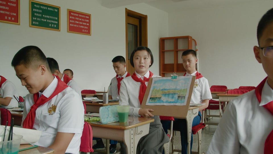 Ein Klassenzimmer. Asiatische Kinder in Schuluniform. Ein Mädchen zeigt eine Zeichnung eines Berges. 