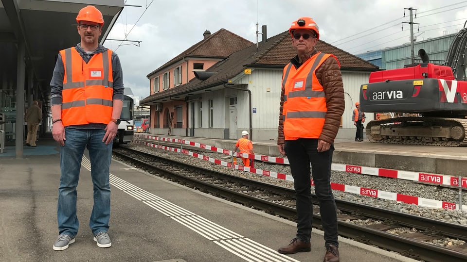 Zwei Männer in orangen Warnwesten stehen auf einem Perron vor dem WSB-Bahnhof in Aarau.