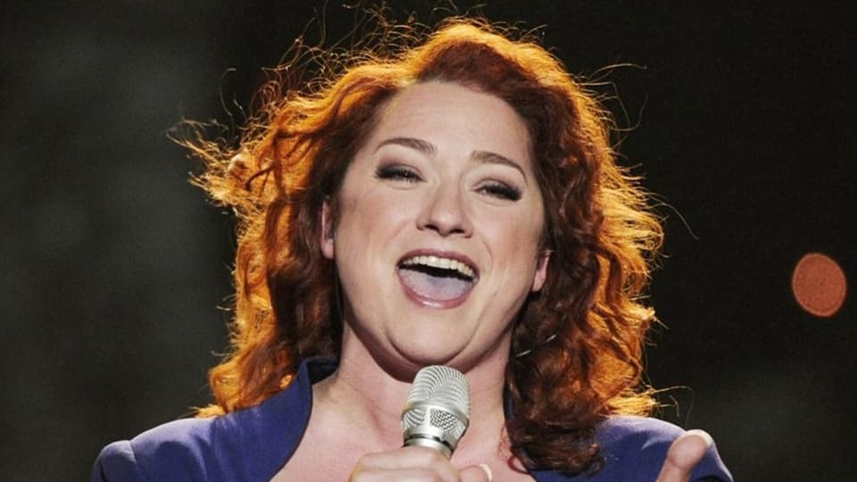 Eine Frau mit roten Haaren steht auf der Bühne und singt. 