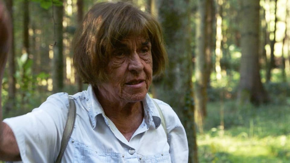 Eine ältere Frau steht im Wald.