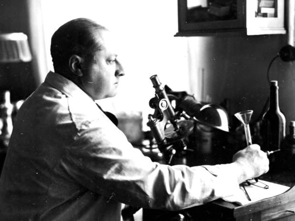 Gottfried Benn im Arztkittel, sitzend vor einem Mikroskop.