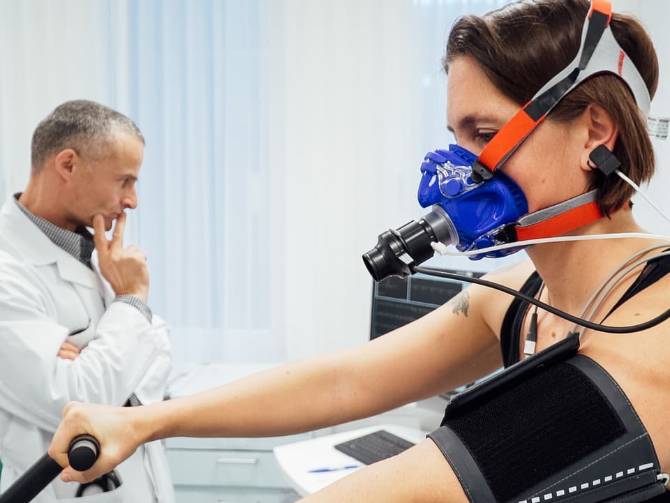 Frau mit Sauerstoffmaske, dahinter ein Arzt
