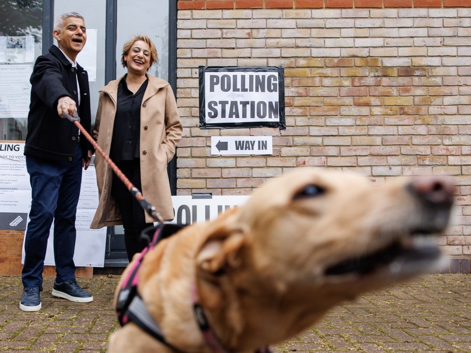 Paar steht mit Hund vor einem Wahllokal
