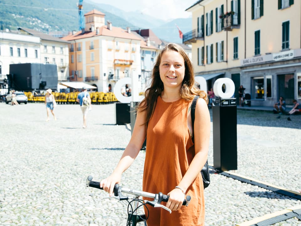 Junge Frau in rötlichem Sommerkleid hält ein Fahrrad