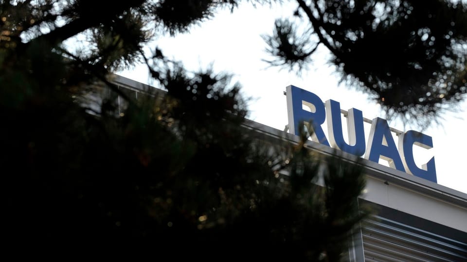 Das Firmenlogo von Ruag auf einen Gebäudedacht, im Vordergrund ein Nadelbaum.
