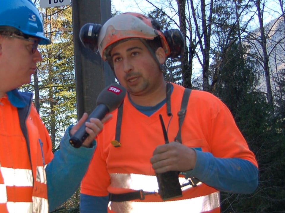 Zwei Männer in Schutzkleidung und mit Helmen während eines Interviews.
