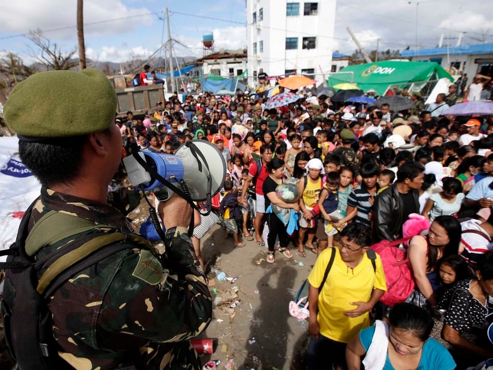 Ein philippinischer Armeeangehöriger auf Tacloban ermahnt die drängende Menschenmenge mit einem Megaphon zu Ruhe und Ordnung