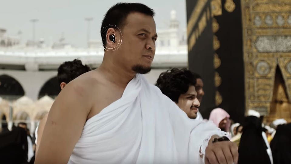 Ein Mann vor der Kaaba in Mekka hat einen Knopf im Ohr.
