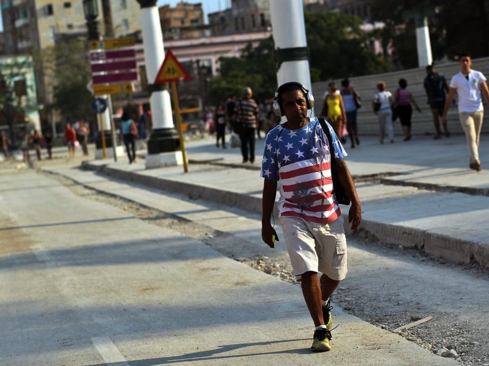Ein junger Kubaner schlendert in einem T-Shirt die Strasse entlang. Auf dem T-Shirt ist die amerikanische Flagge abgebildet