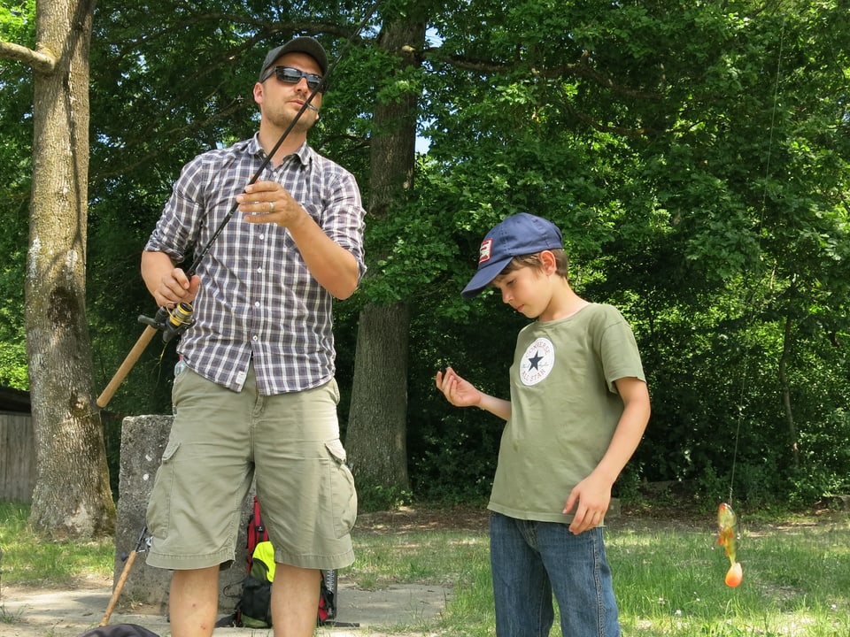 Kursleiter Jon Cavegn rüstet mit einem jungen Teilnehmer die Fischerrute.