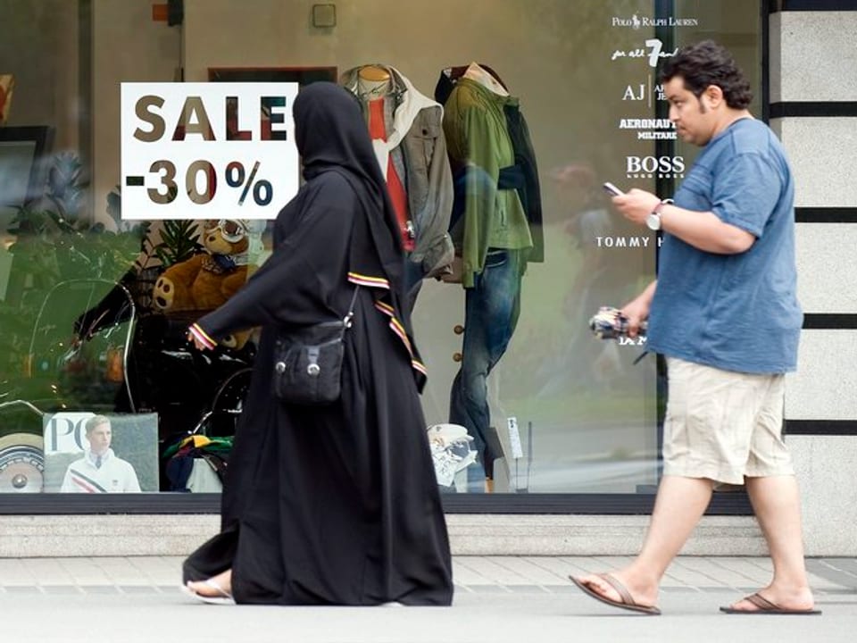 Ein arabisches Ehepaar, die Frau verschleiert, vor einer Interlakner Boutique