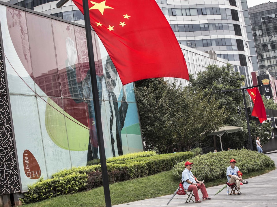 Zwei Personen sitzen unter chinesischer Fahne.
