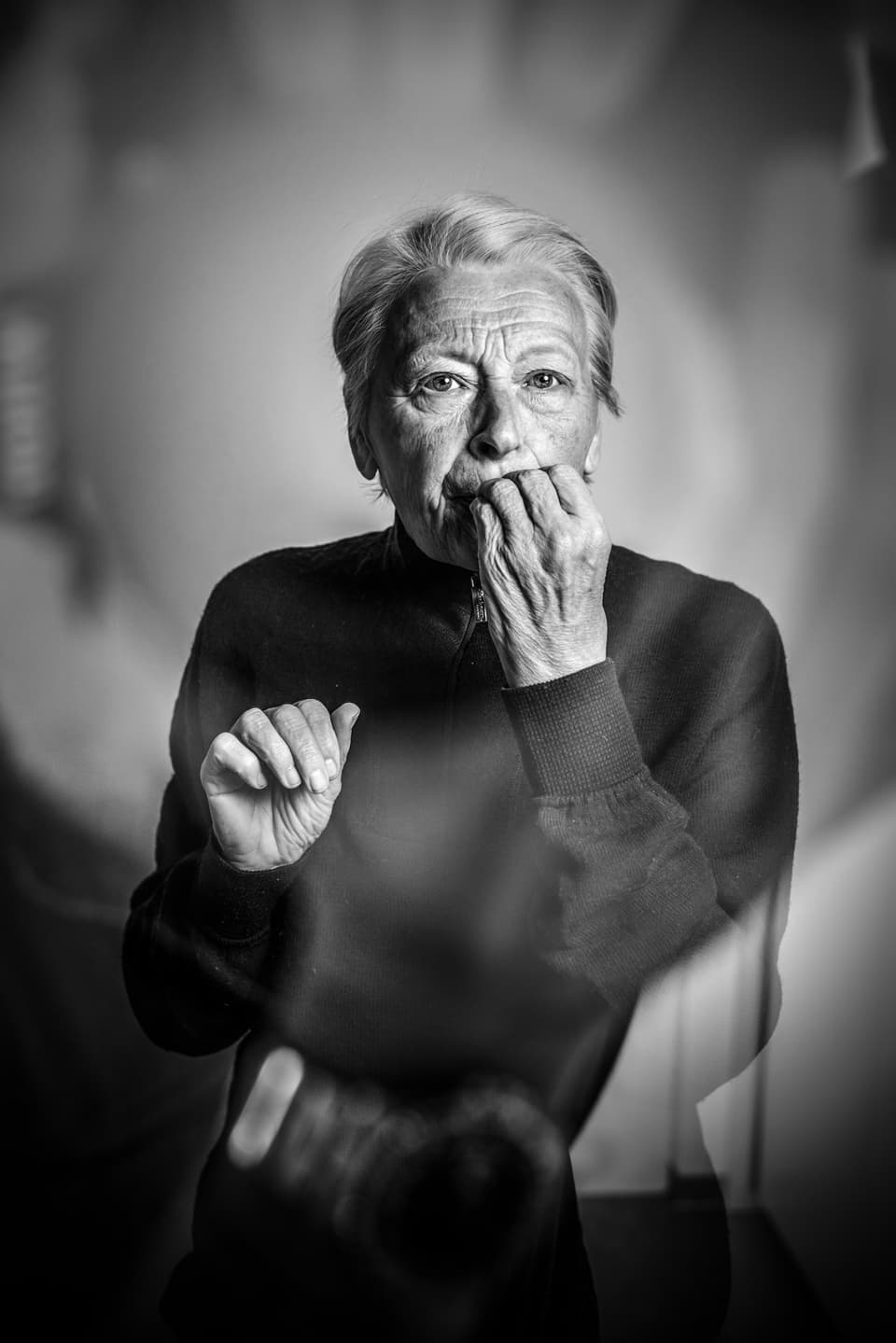 Portrait einer älteren Frau, die die Finger einer Hand im Mund hat. Im Bild ist auch der Schatten des Fotografen zu erkennen.