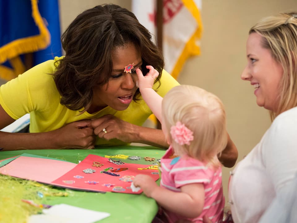 Ein kleines Mädchen klebt Michelle Obama einen Aufkleber ins Gesicht