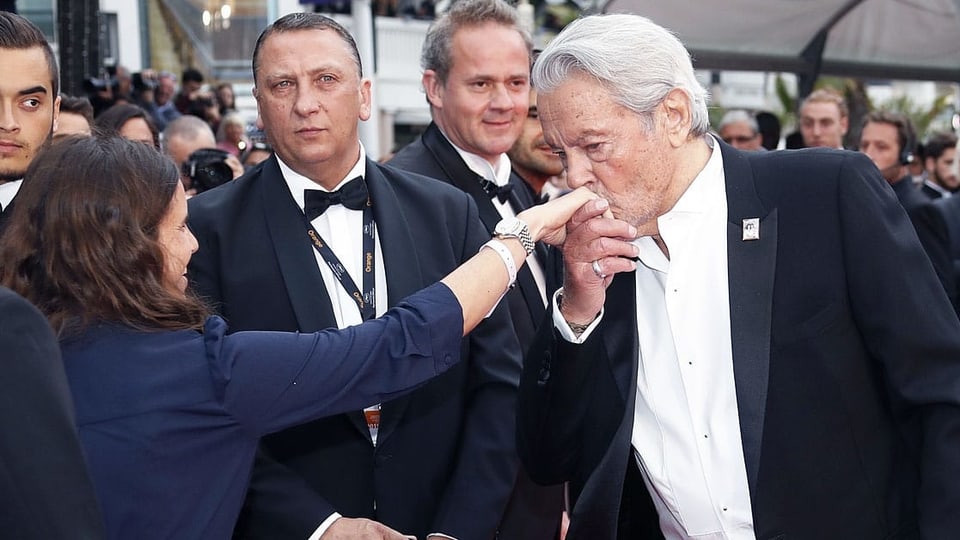 Alain Delon küsst die Hand einer Frau auf dem roten Teppich in Cannes.